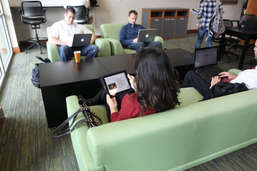 Students with laptops sit in lounge chairs and couches with their laptops in Hough Hall