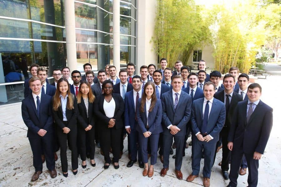Large group of students in business suits pose for a photo outside Hough Hall