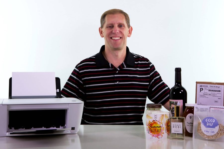 Dave Carmany sitting at a table with a printer and products with labels from his company, OnlineLabels.com.