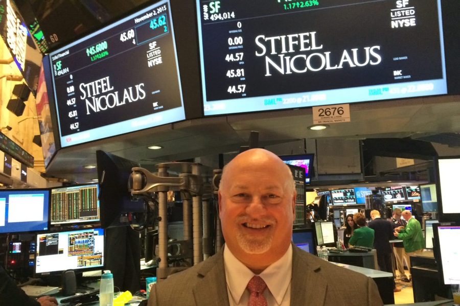 Ben Plotkin poses for a photo on the NYSE stock exchange floor under a sign with the Stifel trading price and analytics.