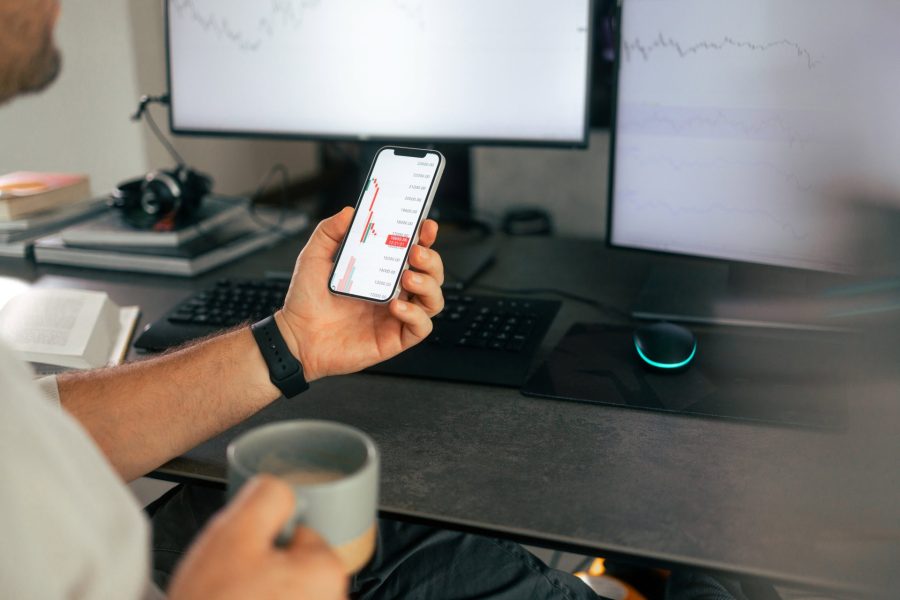 Man holding mobile phone with investment graphics in one hand and a coffee cup in the other hand