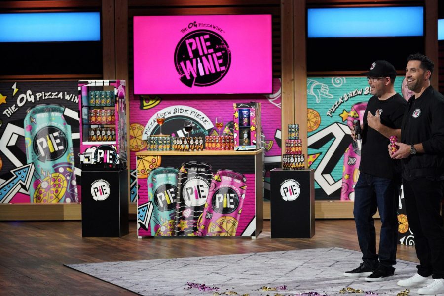 Joshua Green and his business parter in front of a colorful background on the TV show, Shark Tank.