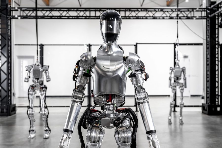 A robot stands at attention while two others stand in the background