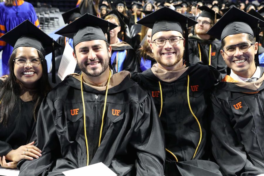 Four students wearing graduation caps and gowns pose for a photo while at graduation.