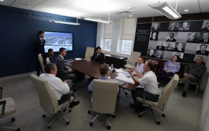 Rick Scarola speaks sitting at a conference table with a group of students listening.