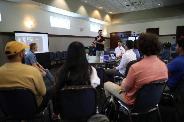 A man stands and talks to others seated in the room.