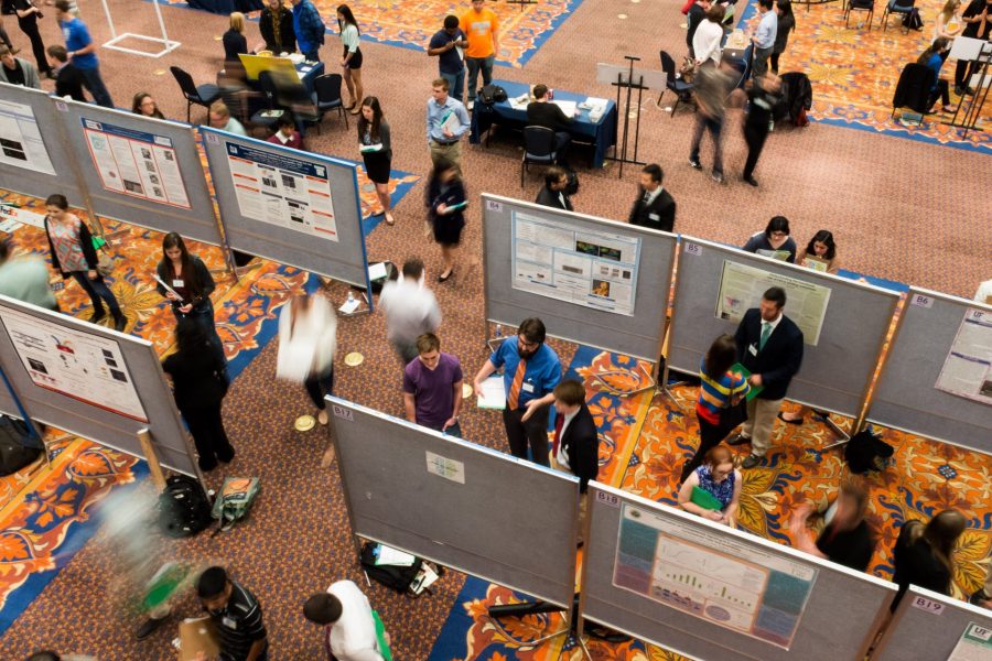 Birds eye view of an undergraduate research event. Large room with student research project posters and people walking around looking at the poster content.