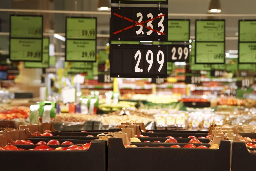 Grocery store price signs hang from ceiling above produce indicating price drop from $3.33 to $2.99.