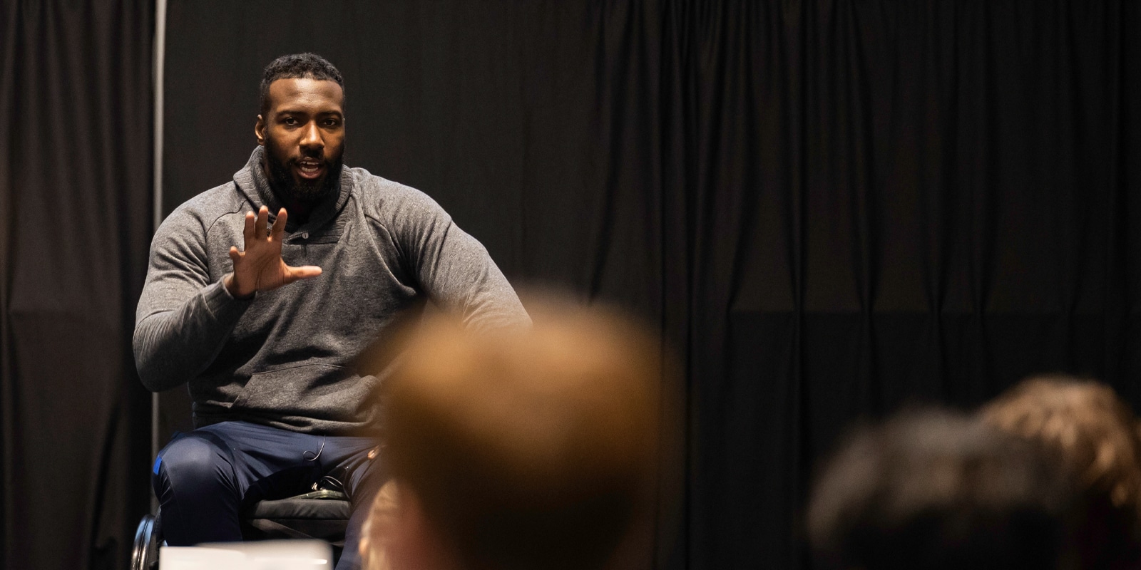 A motivational speaker addresses students from a stage at the Future Advisor Conference, gesturing with one hand during a talk.