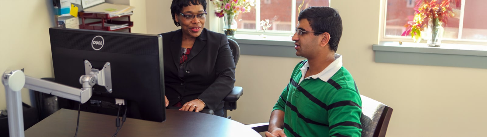 Undergraduate student meets with advisor to discuss academic petition options in a bright, professional office.