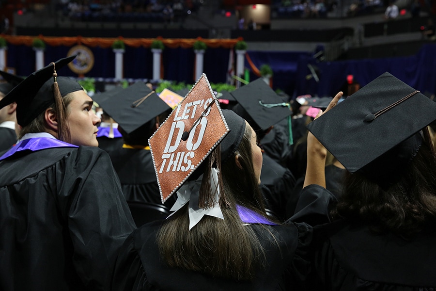 Undergraduate students from the University of Florida Warrington College of Business sit in a row in graduation caps and gowns during commencement