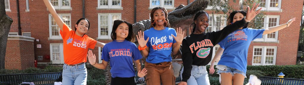 A group of five University of Florida Warrington College of Business students pose in front of the Gator statue while wearing T-shirts displaying their graduation year