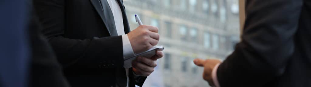 Closeup of business men's hands writing while talking to each other.