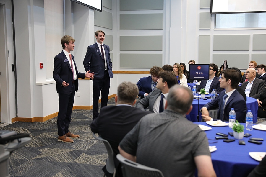 Two students enrolled in a finance and technology class at the University of Florida Warrington College of Business make a presentation to a room full of students in suits