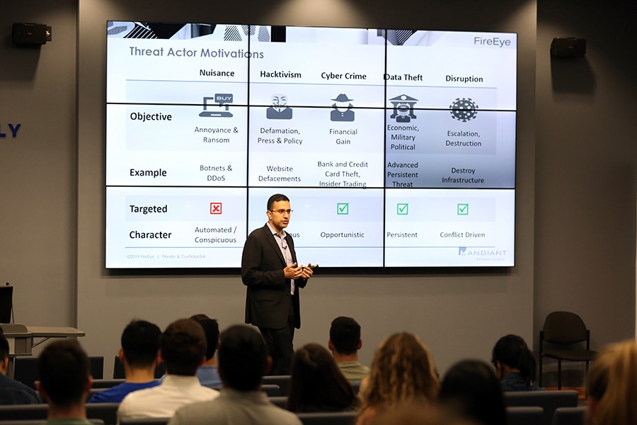 A professor presents on threat actor motivators to a classroom full of graduate and combination degree Information Systems and Management students