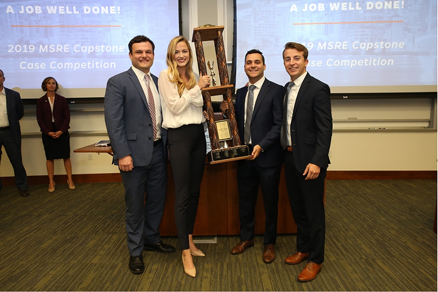Four students, including students enrolled in the combination real estate program, hold up a trophy following a case competition win