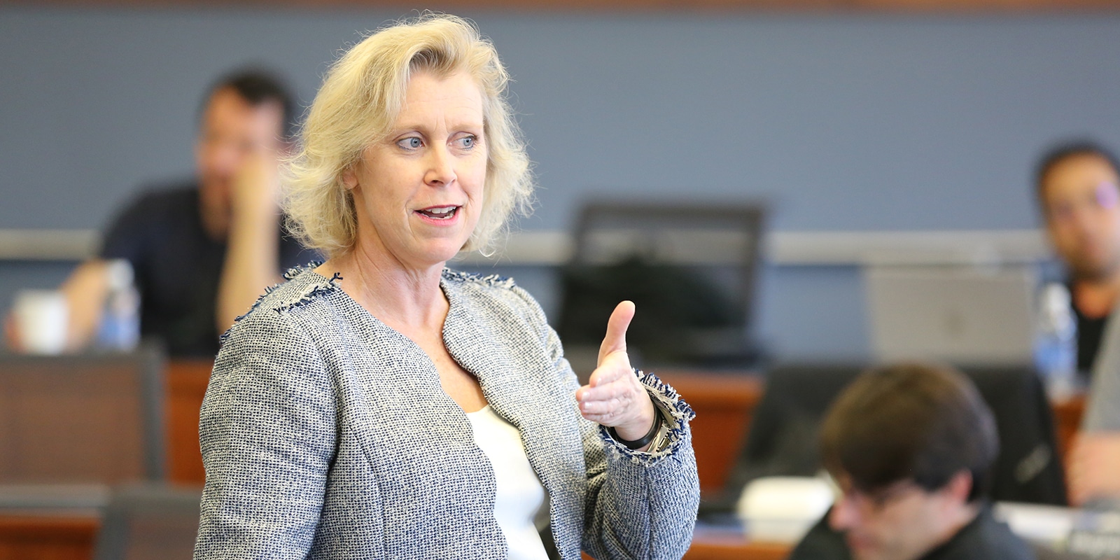 A Warrington faculty member gestures with one hand while explaining an AI and analytics concept to a classroom of Executive MBA students