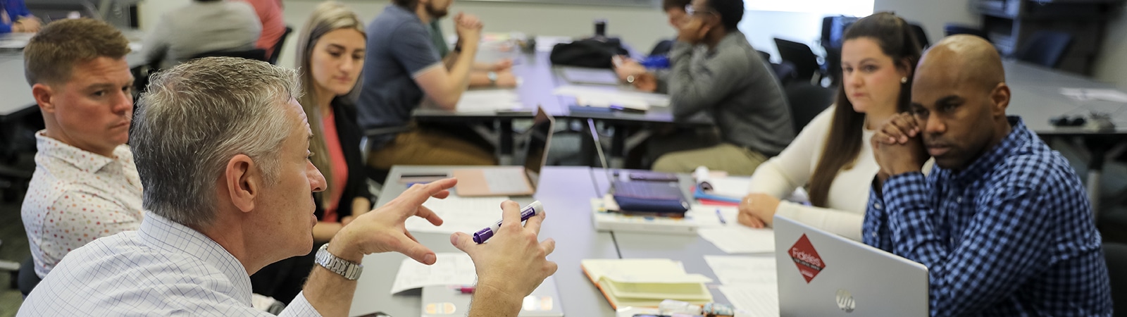 A group of Executive MBA students from UF Warrington engage in a study session while sitting around a table with their laptops