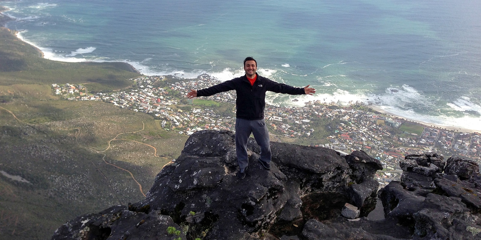During a Global Immersion Experience, a UF Warrington Executive MBA student stands, arms open, on a rocky peak overlooking a city