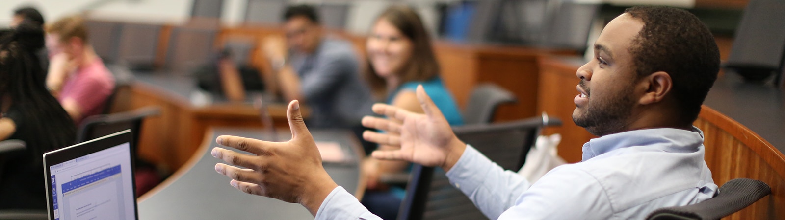 A University of Florida professor sitting in front of a classroom of Full-Time MBA students gestures with his hands while discussing a concept