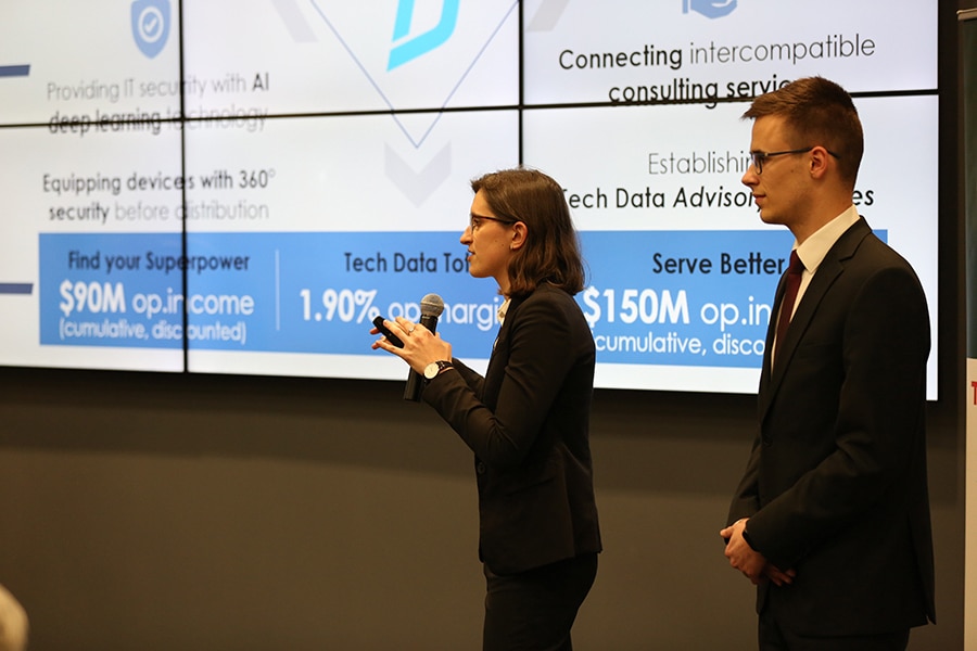 Two University of Florida Warrington College of Business graduate students stand in front of a screen with statistics to make a presentation on their data