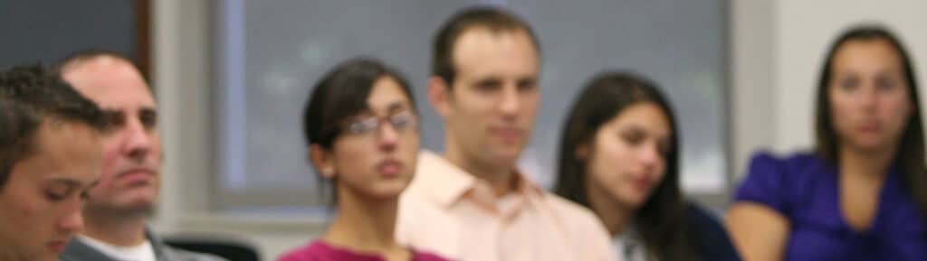 Graduate students from the Warrington College of Business sit in a lecture hall to listen to a professor.