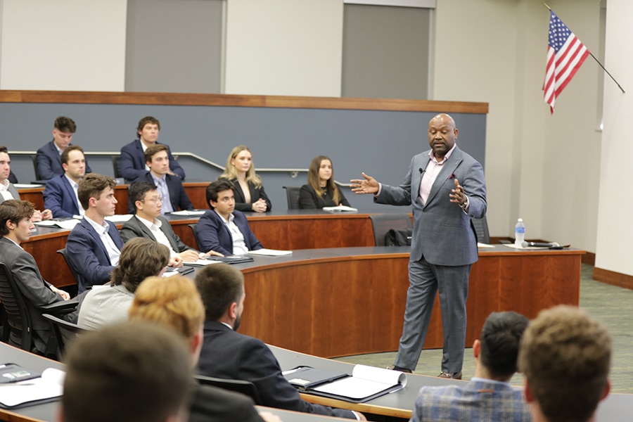 A professional talks to a classroom of University of Florida Warrington College of Business graduate students, all wearing suits, about his career
