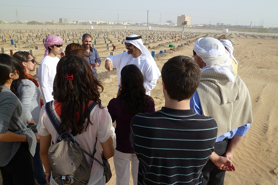 During a study abroad trip, a group of University of Florida Warrington College of Business graduate students meet with a tour guide wearing a shemagh and sunglasses in a desert region