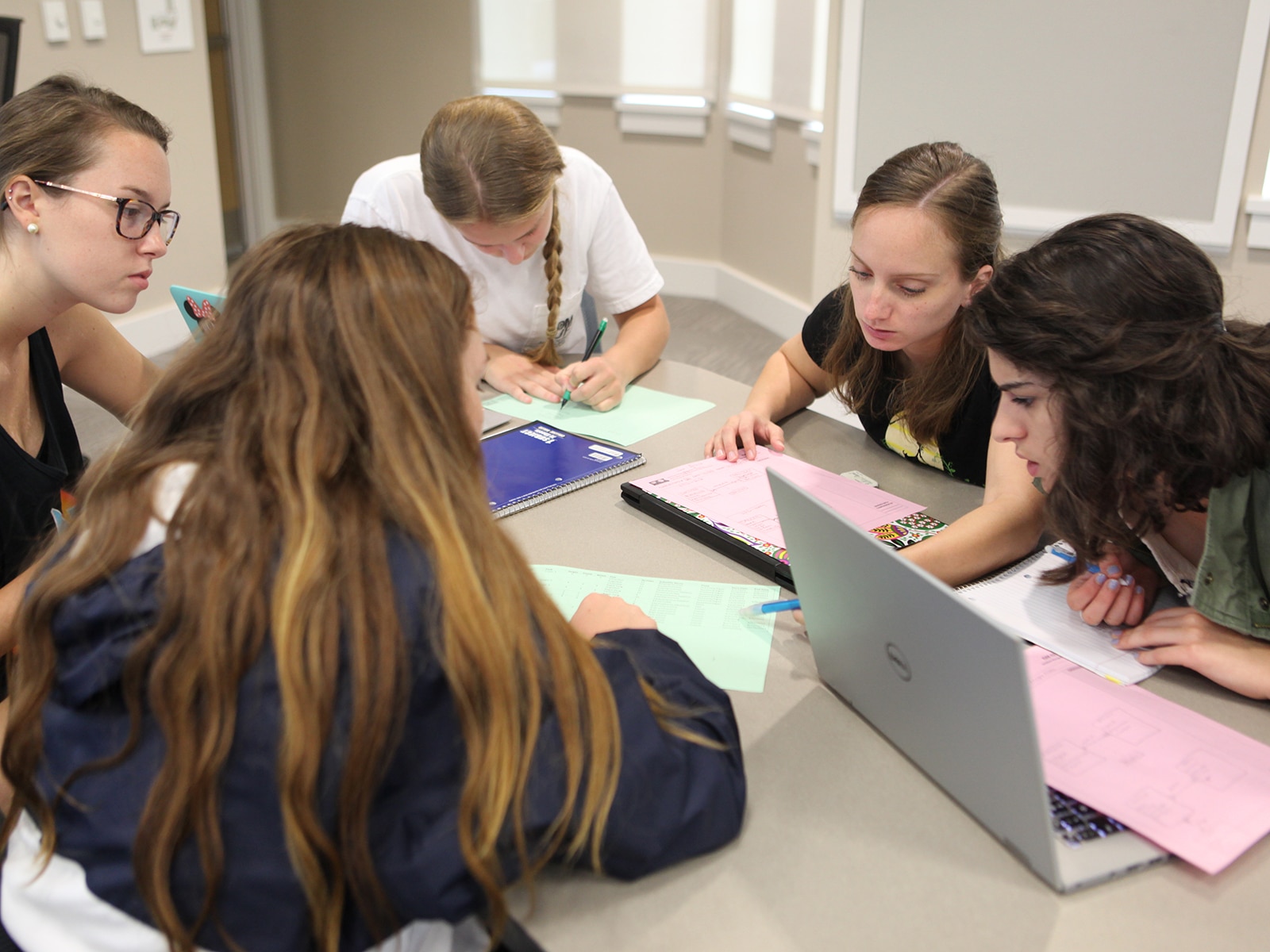 Undergraduate students from the University of Florida Warrington College of Business congregate around a table and use their laptops for a group project