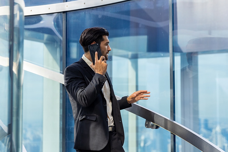 Wearing a suit, a student from the University of Florida Warrington College of Business' MBA/MS in Real Estate uses a phone while looking out a window