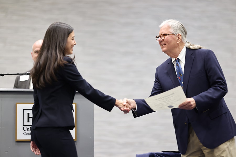 A student enrolled in the UF Warrington College of Business' joint JD/Master of Accounting program shakes hands with a professor while accepting an award certificate