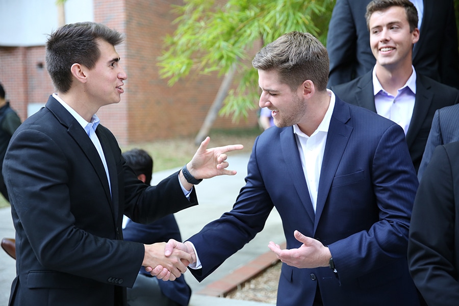 Two UF Warrington College of Business students enrolled in the joint MBA/MS in Real Estate program shake hands while wearing suits