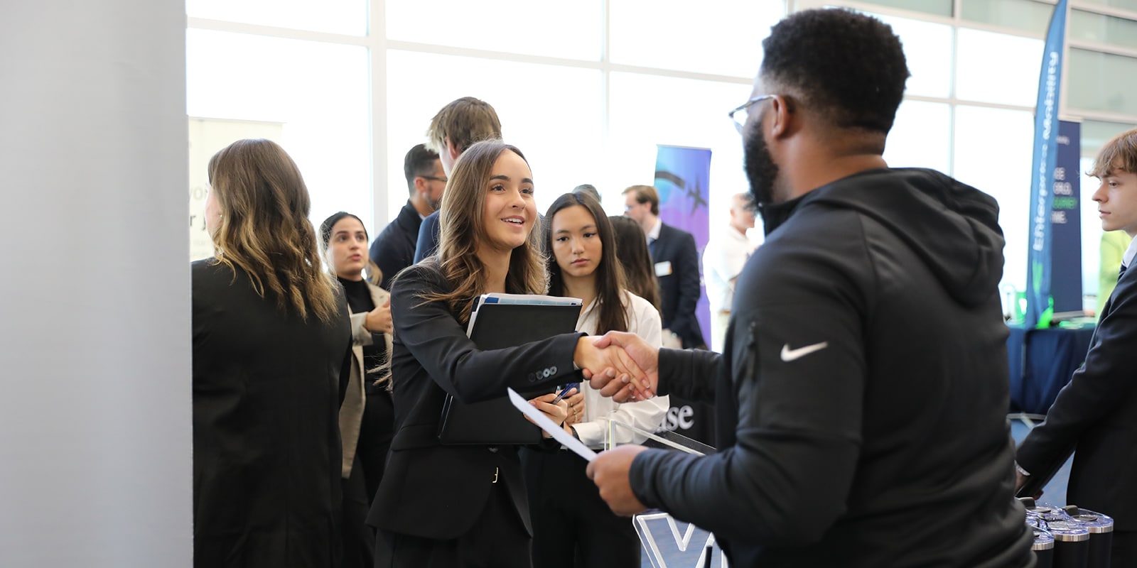 A student from the University of Florida Warrington College of Business' MSM program, holding a folder, shakes hands with a recruiter during a career event
