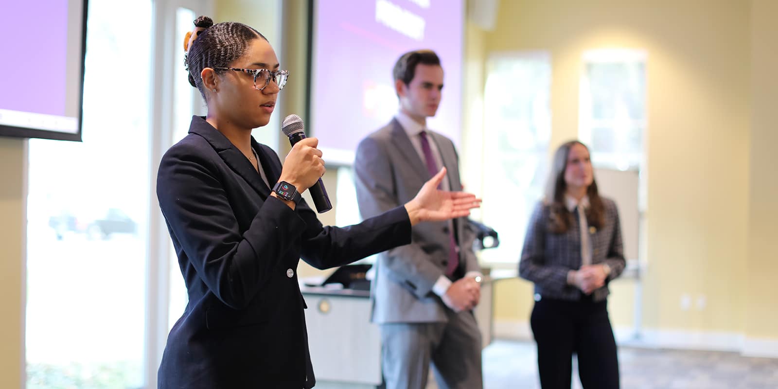 A student from UF Warrington's MSM program holds a microphone and stands in front of a screen to speak about their internship experience