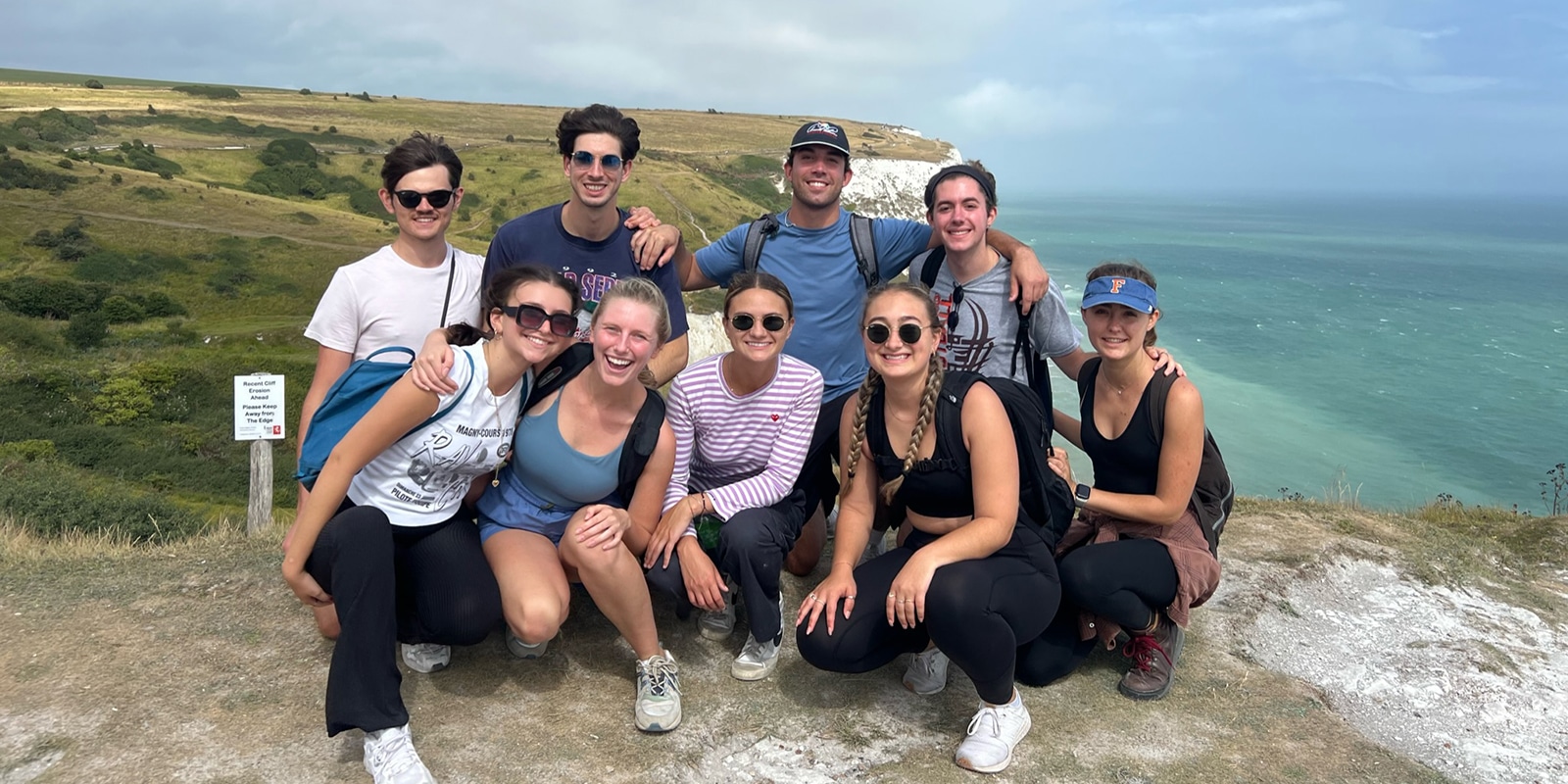 During a study abroad trip, students from UF Warrington's MSM program pose for a photo on a cliff near the ocean and green fields