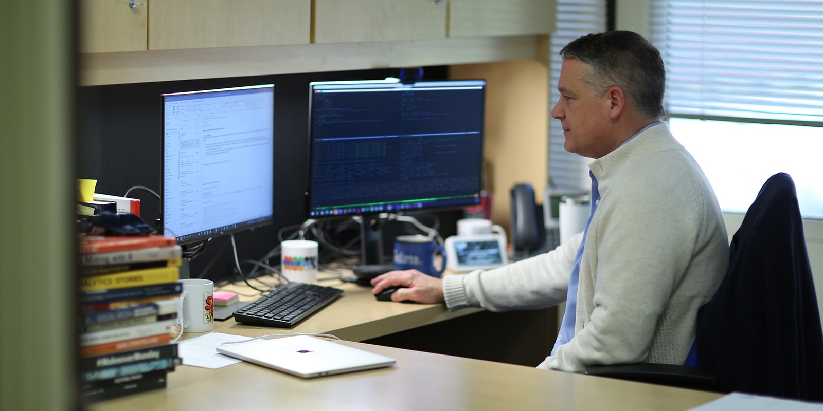 Sitting behind a desk, a faculty member from the University of Florida Warrington College of Business reviews data and code on two computer monitors