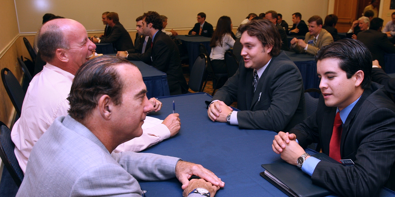 Two current UF Warrington College of Business students wearing suits have a conversation with two alumni on the other side of a table