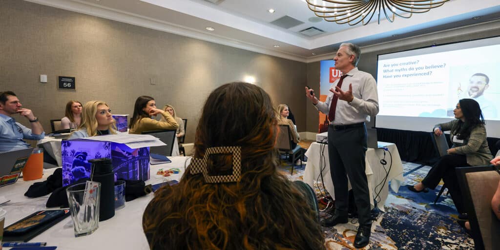 A speaker stands in front of a screen with a slide during a presentation geared toward University of Florida MBA students during a Summit Series event