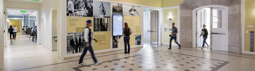 University of Florida Warrington College of Business undergraduates walk through the interior of a building with tiled floors and photos on the walls.