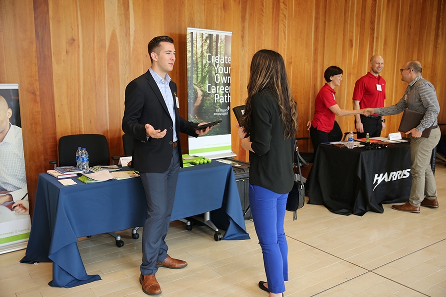 A networking event at the University of Florida Warrington College of Business, where students engage with company representatives at career fair booths.
