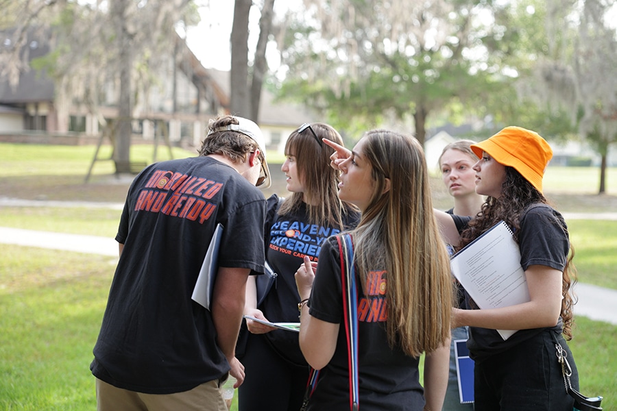 A group of Warrington College of Business students participating in a leadership development program on the University of Florida campus, holding notebooks and engaging in conversation.