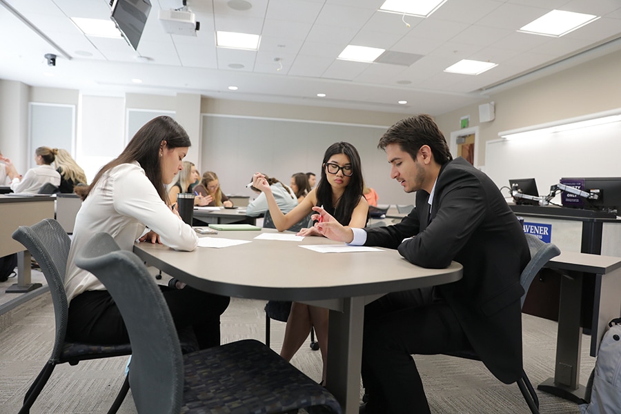 Students collaborating around a table in a classroom at the University of Florida Warrington College of Business, discussing and writing notes.