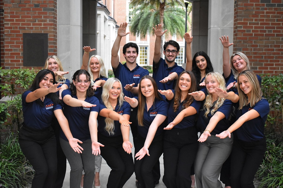 A group of Warrington College of Business students wear matching shirts as they pose in front of a brick building on the University of Florida campus.