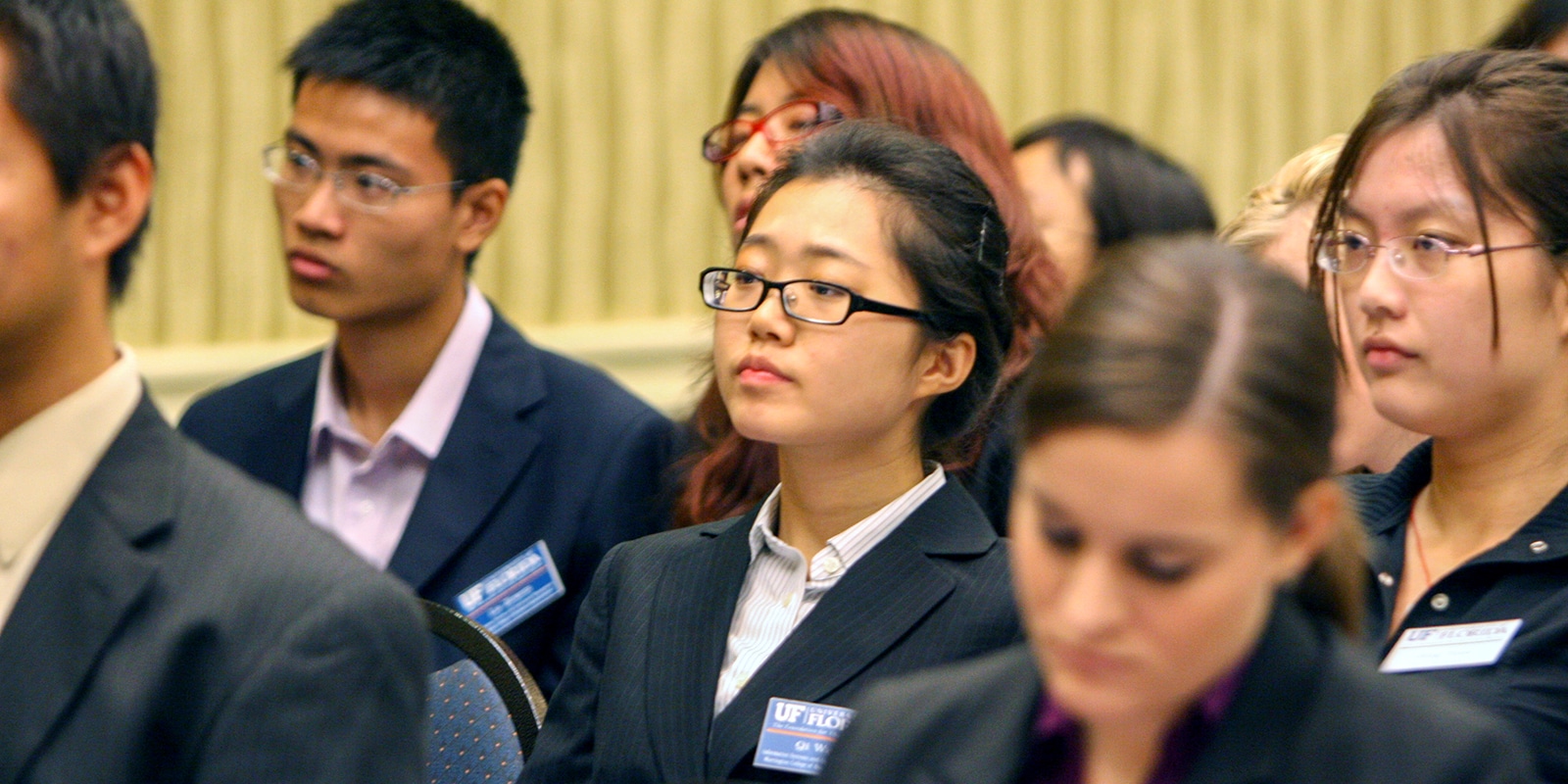 Wearing suits and name tags, a group of UF Warrington Weekend Part-Time MBA students watch a presentation from the audience.