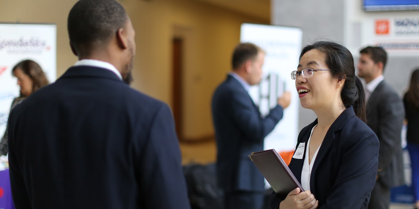A student has a conversation with a prospective employer at a networking event at the University of Florida Warrington College of Business, with information booths in the background.