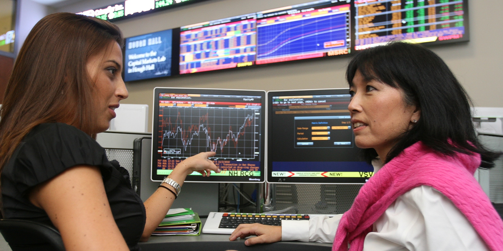 A female student pointing at a Bloomberg terminal monitor. 