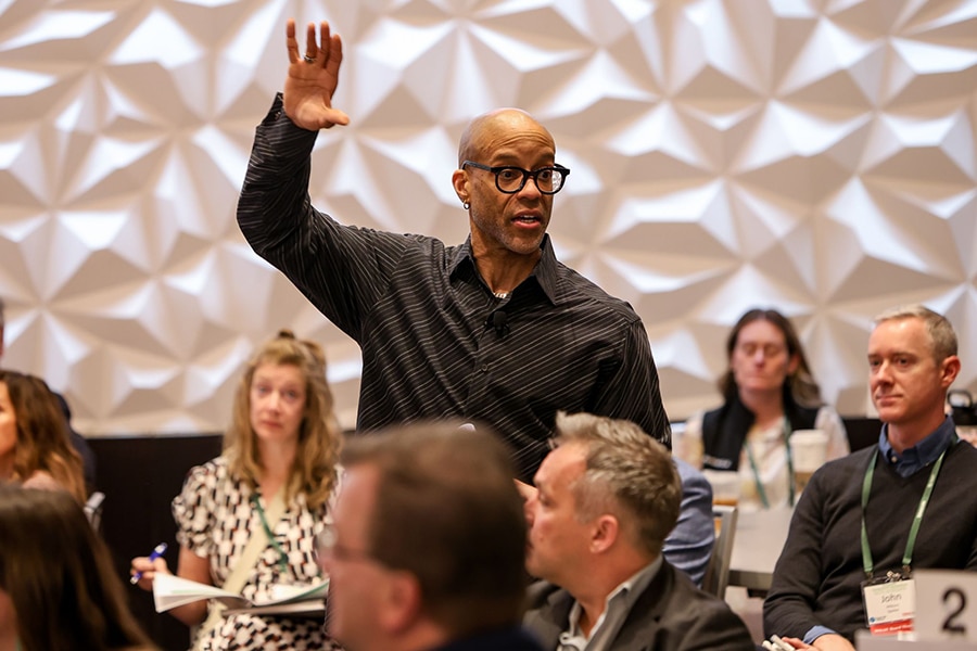 Warrington Alumni Americus Reed (Ph.D. ’00) stands among an audience with one hand raised