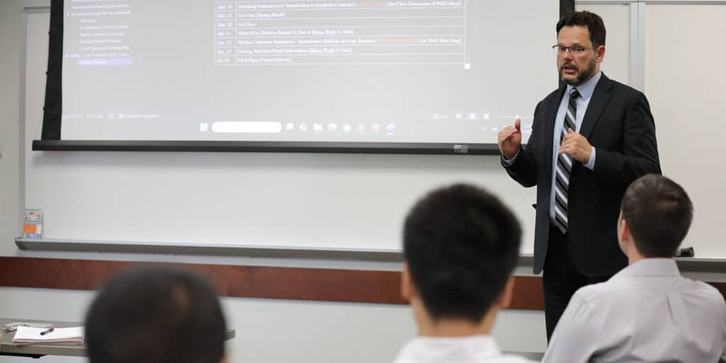 A professor explains a data analytics concept while standing in front of a screen displaying code to a classroom of students from Warrington's BABA in General Studies program