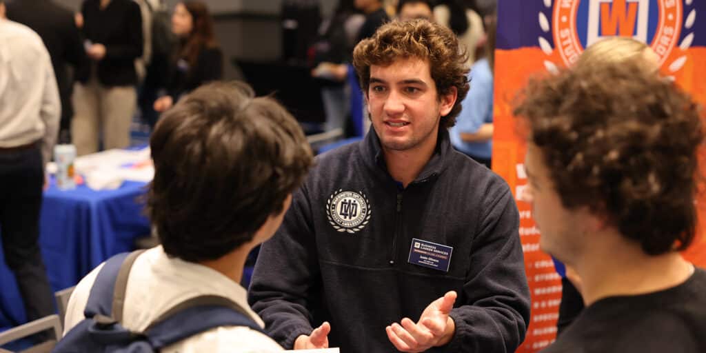 A student organization representative talks to a group of UF Warrington BABA students during a fair for clubs and activities