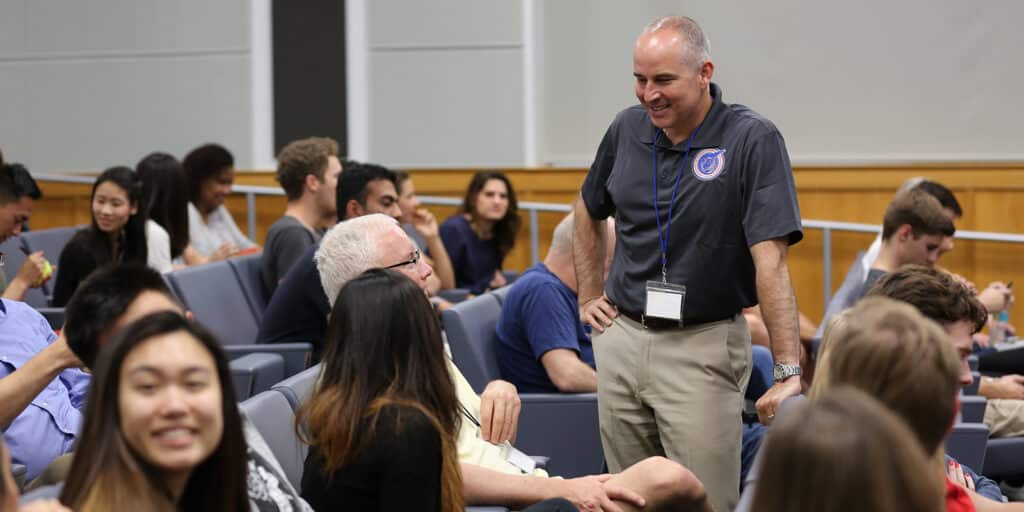 Corporate sponsors and UF Warrington students, including from the BSBA in Information Systems program, wait and converse in an auditorium ahead of a case competition